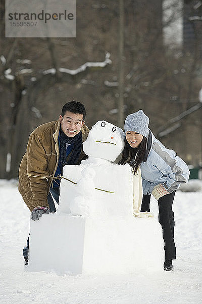 Porträt eines jungen Paares  das neben einem Schneemann steht