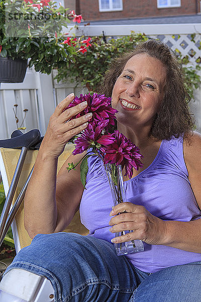 Frau mit Spina Bifida riecht an den Blumen auf der Gartenterrasse