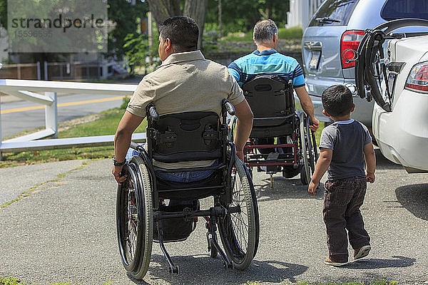 Freunde mit Rückenmarksverletzungen in Rollstühlen mit einem Kind auf einem Parkplatz