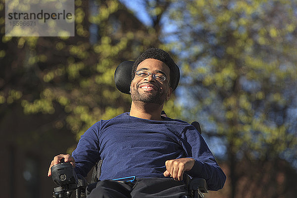 Glücklicher afroamerikanischer Mann mit Cerebralparese  der draußen seinen Elektrorollstuhl benutzt