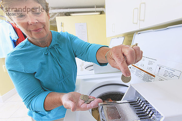 Ältere Frau  die Geld in eine gewerbliche Waschmaschine steckt