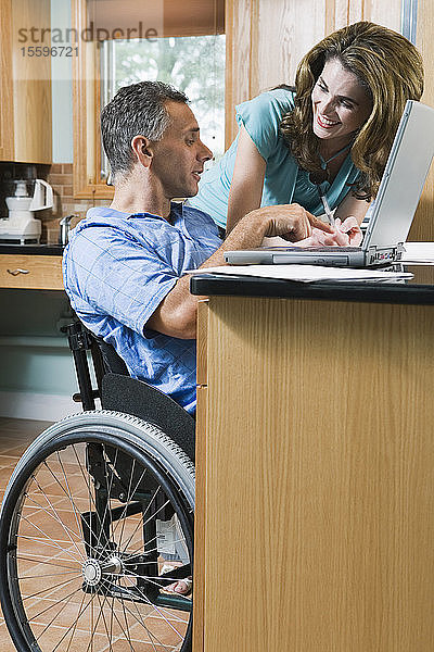 Seitenprofil eines reifen Mannes  der in einem Rollstuhl sitzt  mit einer lächelnden  neben ihm stehenden Frau mittleren Alters
