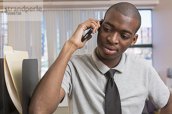 Afroamerikanischer Mann mit Autismus  der in einem Büro mit einem Handy telefoniert