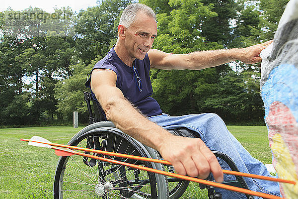 Mann mit Rückenmarksverletzung im Rollstuhl entfernt Pfeile von der Zielscheibe nach einem Bogenschießtraining