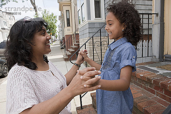 Hispanische Frau spielt mit ihrer Tochter vor ihrem Haus