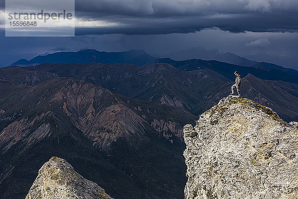 Ein Wanderer steht im Sonnenschein auf dem Gipfel des Sukakpak Mountain  während Sturmwolken über der Brooks Range aufziehen; Alaska  Vereinigte Staaten von Amerika