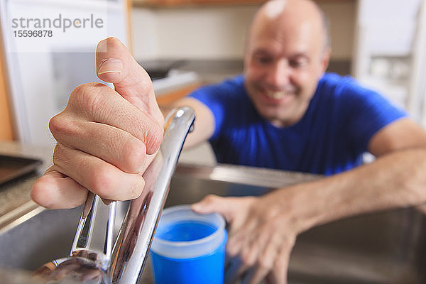 Mann mit Friedreich-Ataxie und deformierten Händen benutzt seinen Wasserhahn in der Küche
