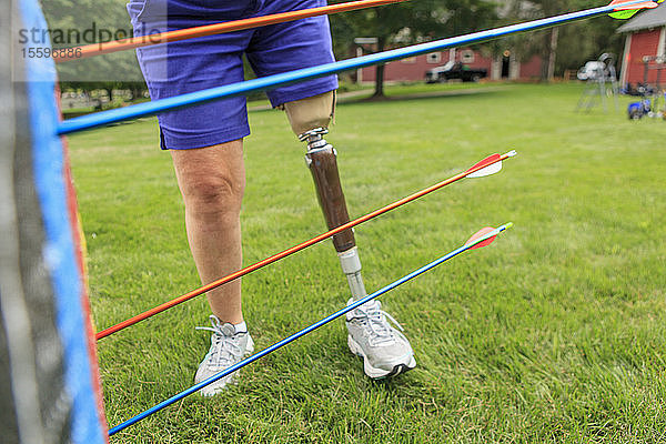 Frau mit Beinprothese  die nach einem Bogenschießtraining Pfeile von der Zielscheibe zieht