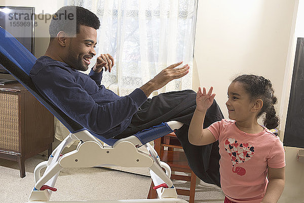 Glücklicher afroamerikanischer Mann mit zerebraler Lähmung  der mit seiner Tochter zu Hause spielt