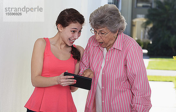 Lächelnde ältere Frau und ihre Enkelin  die ein digitales Tablet benutzt