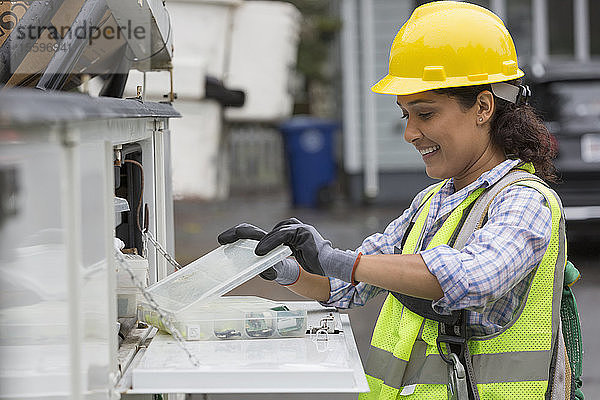 Hispanische Mitarbeiterin eines Versorgungsunternehmens mit einer Kiste mit Kabelverstärkern auf einer Baustelle