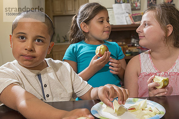 Hispanischer Junge mit Autismus isst mit seinen Schwestern zu Hause einen Apfel