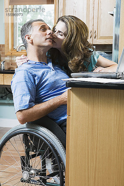 Mid adult woman kissing a mid adult man sitting in a wheelchair