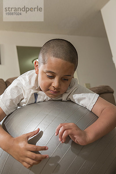 Hispanischer Junge mit Autismus spielt mit einem Gymnastikball im Wohnzimmer