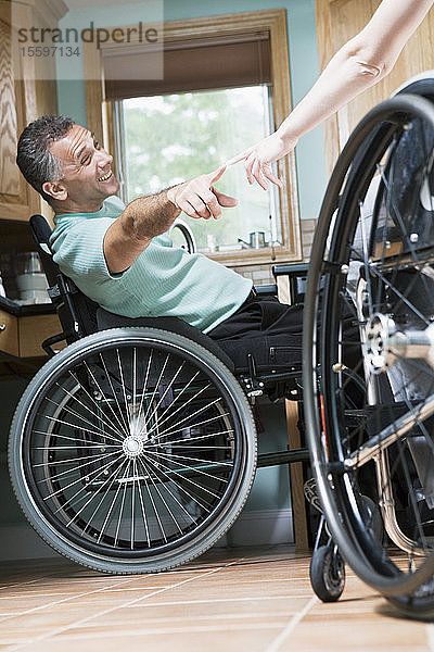 Mittelgroßer erwachsener Mann  der in einem Rollstuhl sitzt und nach dem Finger einer anderen Person greift