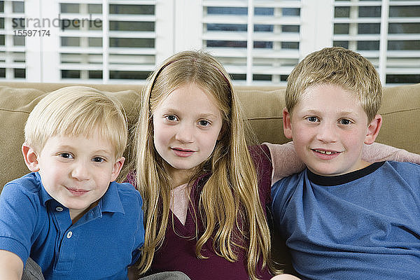 Porträt von drei Kindern  die auf einem Sofa sitzen.