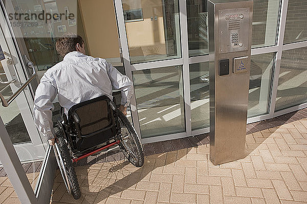 Geschäftsmann mit Querschnittslähmung im Rollstuhl beim Betreten eines Bürogebäudes