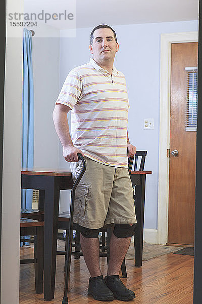 Mann nach einer Operation des vorderen Kreuzbandes (ACL) mit Stock und Kniestütze zu Hause