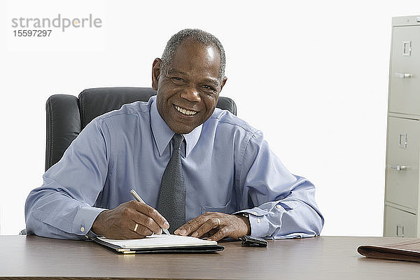 Porträt eines Geschäftsmannes  der auf ein Blatt Papier schreibt und lächelt