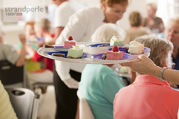 Nahaufnahme der Hand einer älteren Frau  die einen Teller mit Desserttellern bei einem Damenmittagessen hält