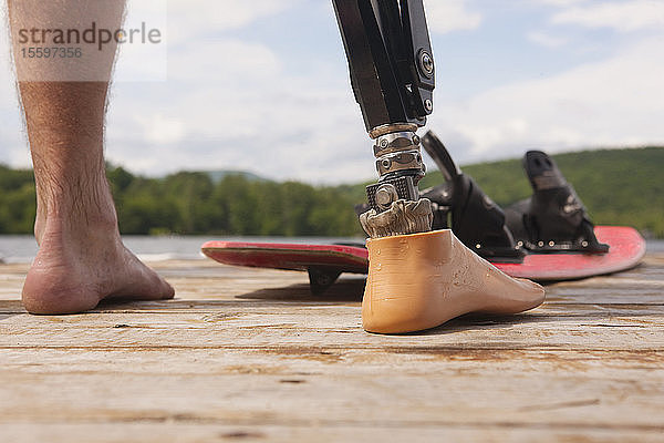 Sportler mit Beinprothese und Wasserskibrett auf einem Steg