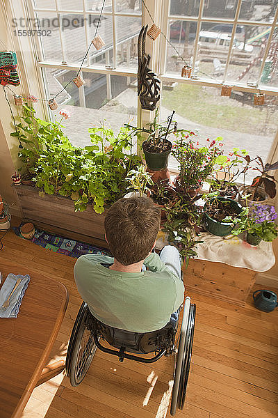 Frau mit Multipler Sklerose im Rollstuhl schaut aus dem Fenster ihrer barrierefreien Wohnung