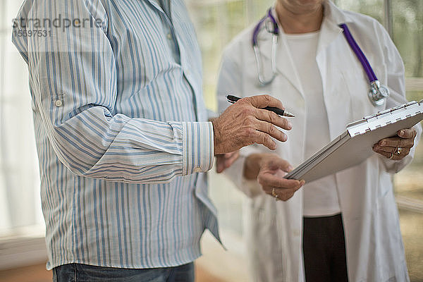 Hände einer Ärztin  die ein Klemmbrett hält  neben einem männlichen Kollegen  der einen Stift hält