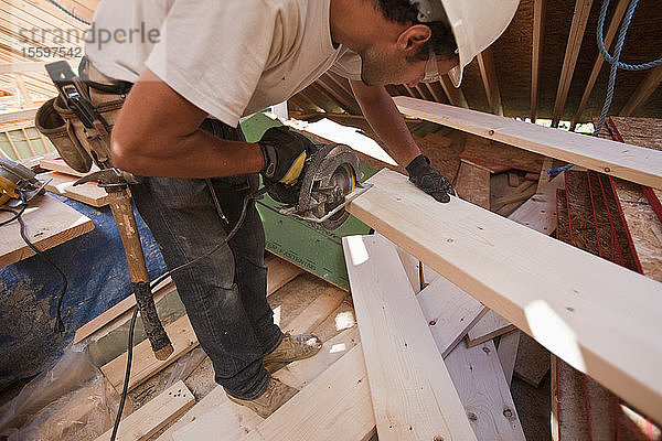 Ein spanischer Zimmermann arbeitet mit einer Kreissäge an einem Dachsparren eines im Bau befindlichen Winkelhauses