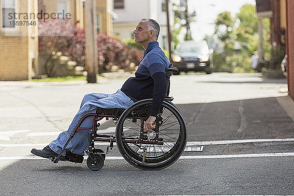 Mann mit Rückenmarksverletzung überquert die Straße in seinem Rollstuhl