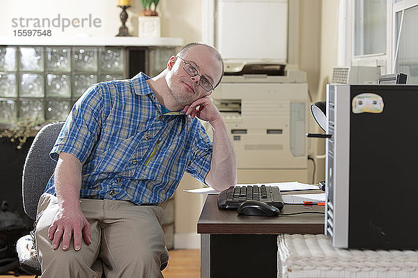 Mann mit Down-Syndrom sitzt an seinem Computer in einem Büro