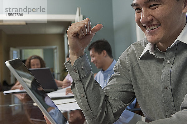 Geschäftsmann  der einen Laptop benutzt  mit seinen Kollegen im Hintergrund in einem Sitzungssaal