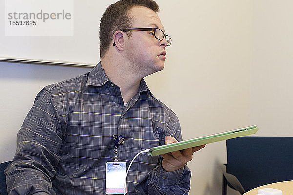 Krankenhausmitarbeiter mit Down-Syndrom benutzt ein Tablet im Büro