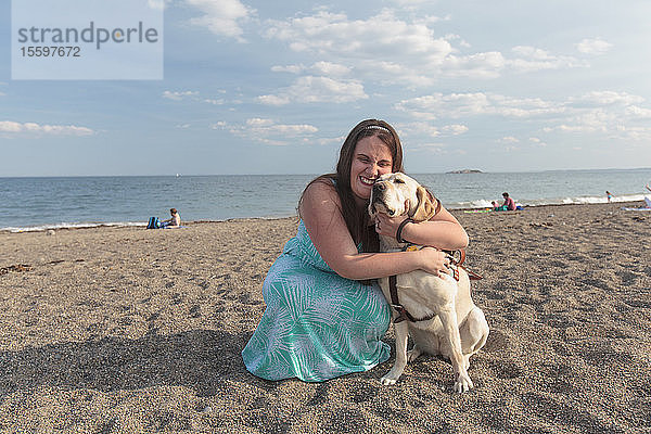 Junge Frau mit Sehbehinderung und ihr Diensthund umarmen sich am Strand