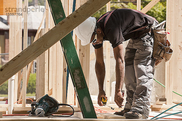 Zimmermann beim Messen mit einem Maßband auf einer Baustelle