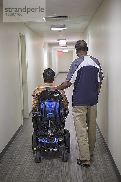 Mann mit Guillain-Barre-Syndrom im Wohnungsflur auf einem elektrischen Stuhl mit seinem Vater