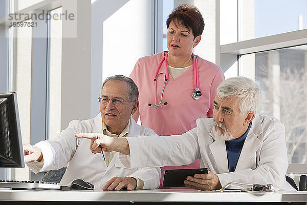 Zwei Ärzte und eine Krankenschwester diskutieren an einem Computer und einem Tablet. Ein Arzt hat Muskeldystrophie