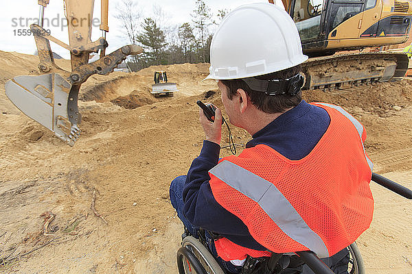 Ein Bauingenieur mit einer Rückenmarksverletzung spricht über ein tragbares Funkgerät mit den Maschinisten