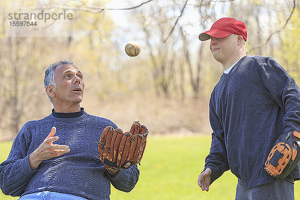 Vater mit Rückenmarksverletzung und sein Sohn mit Down-Syndrom spielen Baseball im Park