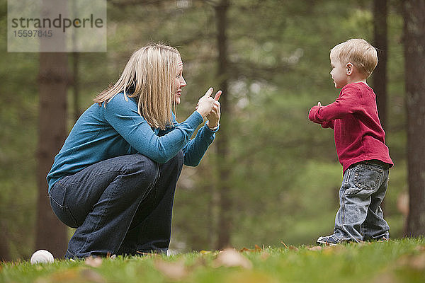 Frau  die das Wort Game in amerikanischer Gebärdensprache gebärdet  während sie mit ihrem Sohn in einem Park kommuniziert