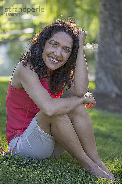 Porträt einer glücklichen hispanischen Frau  die in einem Park sitzt