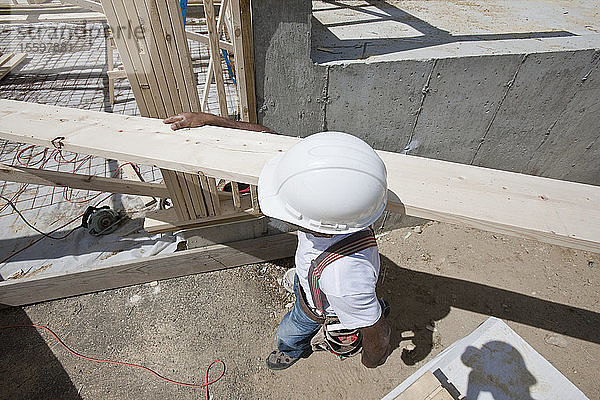 Zimmermann trägt eine Planke auf einer Baustelle