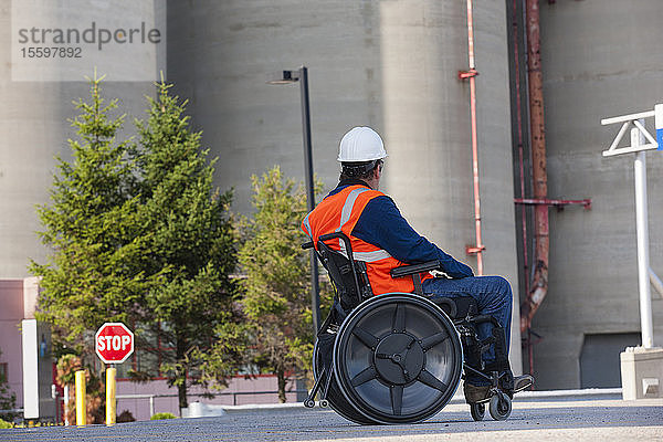 Gebäudetechniker im Rollstuhl bei der Untersuchung von Schüttgutlagertanks im Freien