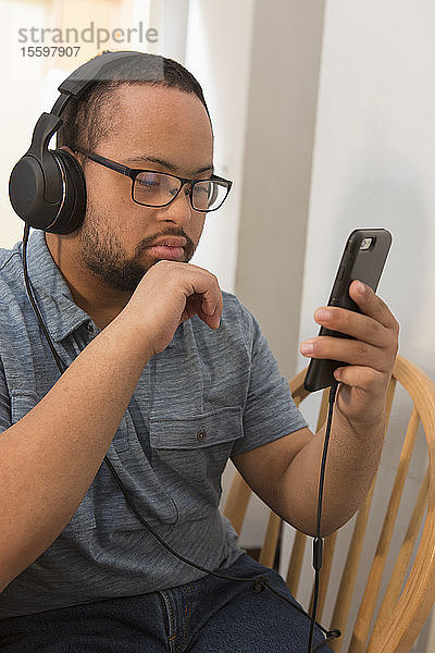 Afroamerikanischer Mann mit Down-Syndrom hört zu Hause mit Kopfhörern Musik am Telefon