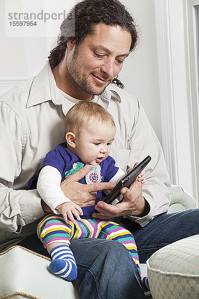 Vater und Baby schauen zu Hause auf ein elektronisches Tablet