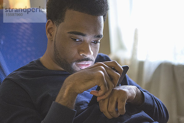 Afroamerikanischer Mann mit zerebraler Lähmung benutzt zu Hause sein Mobiltelefon