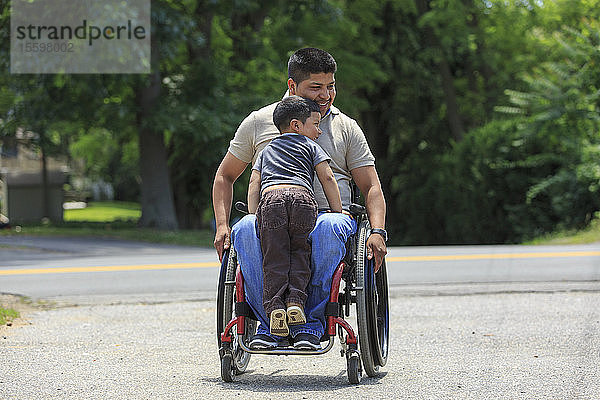 Hispanoamerikanischer Mann mit Rückenmarksverletzung im Rollstuhl mit seinem Sohn