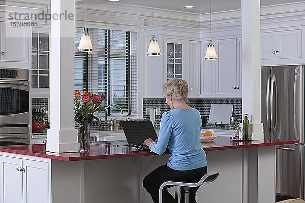 Frau am Laptop in der Küche eines Green Technology Home mit energieeffizienten Geräten  Arbeitsplatten aus Stein und recyceltem Holz