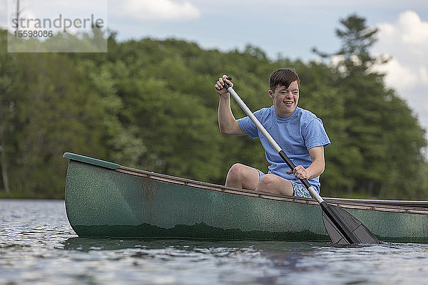 Junger Mann mit Down-Syndrom rudert ein Kanu auf einem See