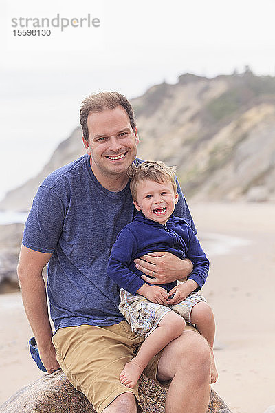 Porträt eines Mannes  der mit seinem Sohn am Strand sitzt