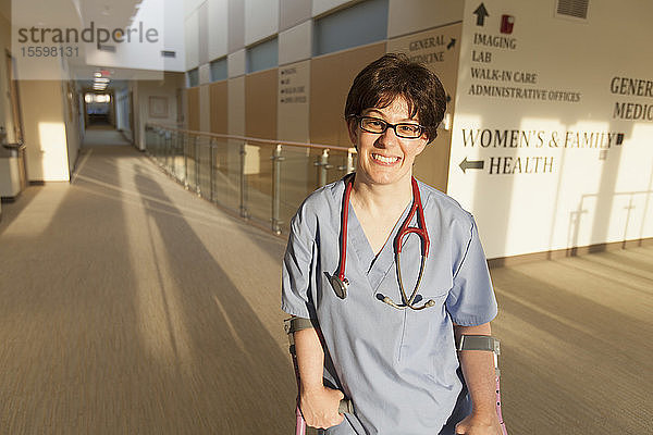 Krankenschwester mit Cerebralparese geht mit ihren Stöcken den Flur einer Klinik entlang